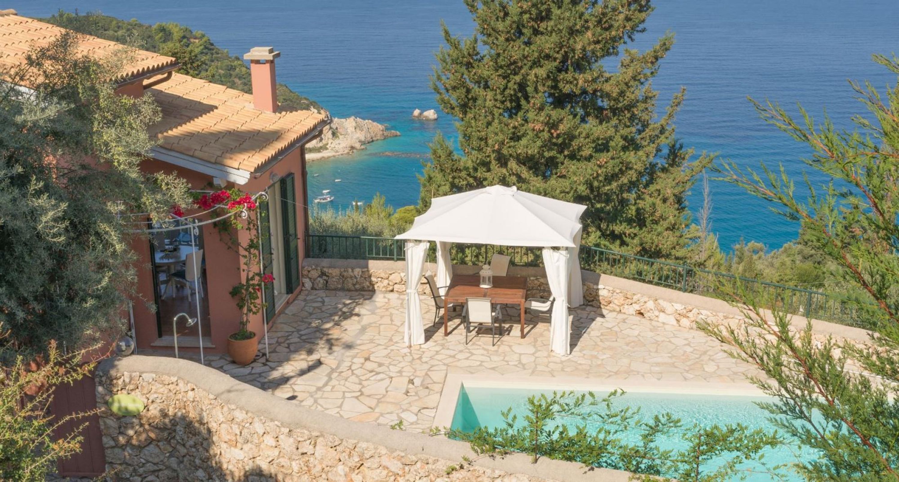 Un patio de piedra con piscina, un pabellón y vista al mar.