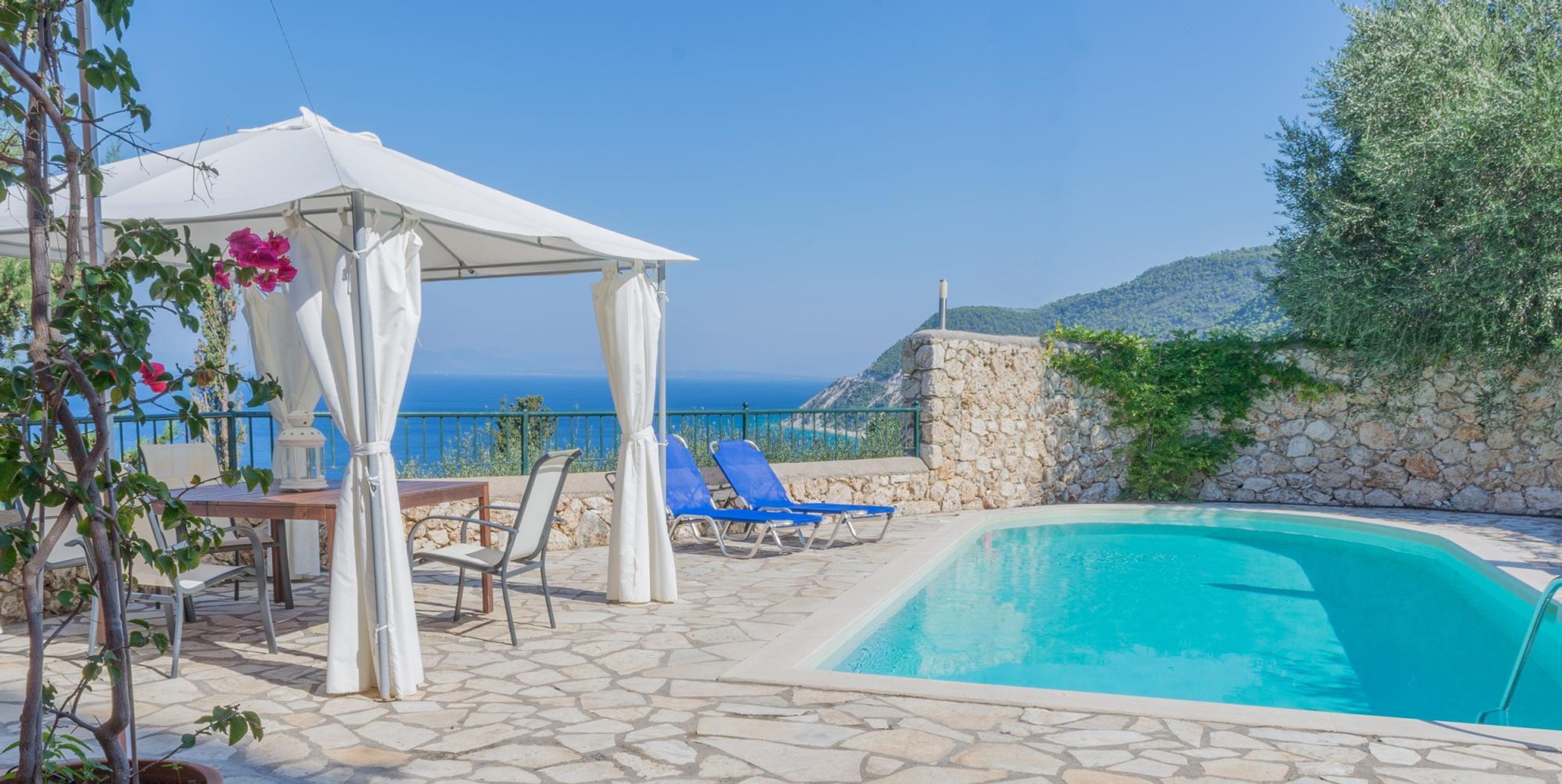 A pool area with a stone floor, a white gazebo, and blue lounge chairs.
