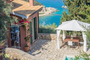 Une terrasse en pierre avec une table et des chaises, un parasol blanc et une vue sur la mer.