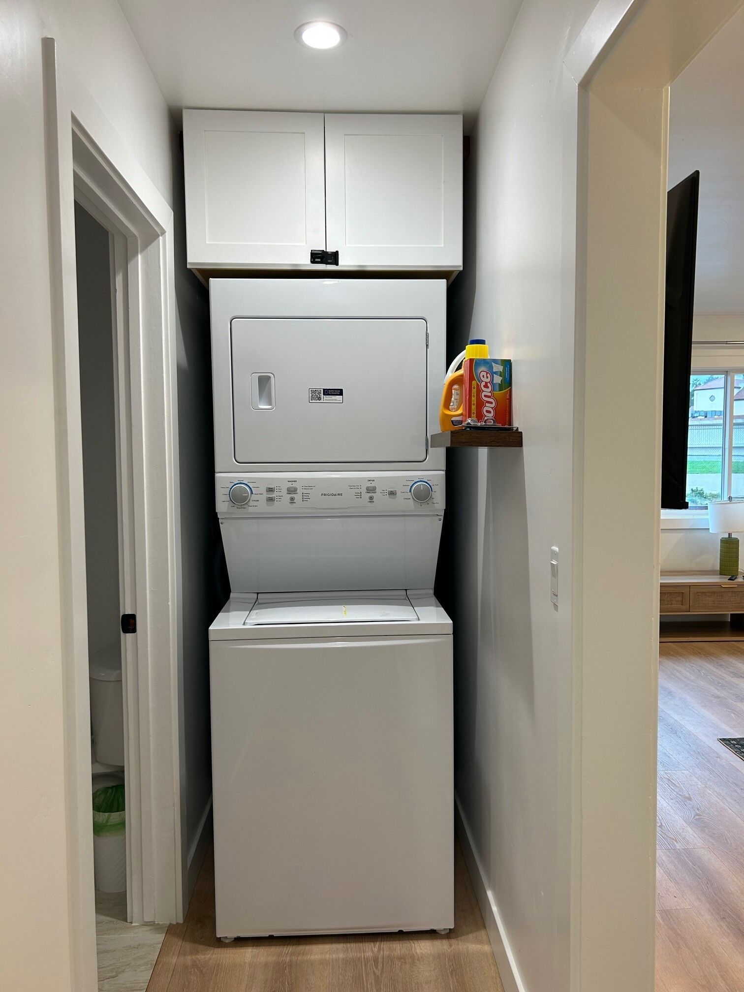 Een functionele wasruimte met een voorlader wasmachine en droger, een klein plankje met wasmiddel, en een deur naar een andere kamer.