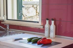 Eine Küchenarbeitsplatte mit einem Messer, Gurken und einer roten Paprika. Auf der Arbeitsplatte stehen zwei Flaschen mit den Aufschriften 'Country Home Olivenöl' und 'Country Home Essig'.