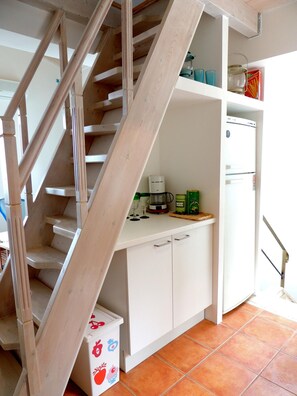 Eine Küche mit Holzentreppe, weißen Schränken und einem kleinen Kühlschrank.