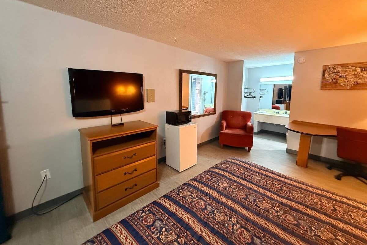 A room with a television, a red chair, a patterned rug, and a small white refrigerator.