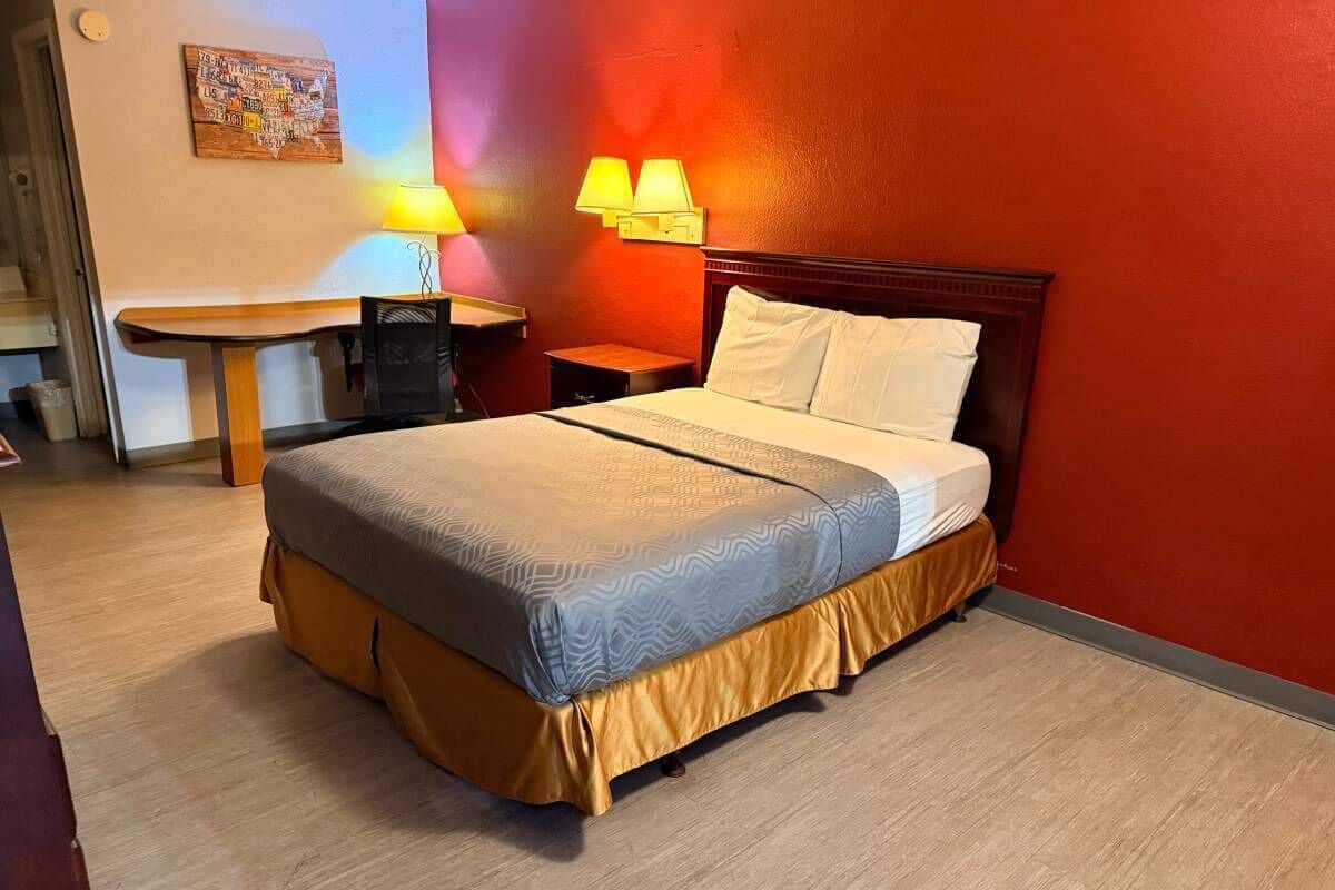A hotel room with a bed, two bedside lamps, a small table, and a wall with a map artwork.