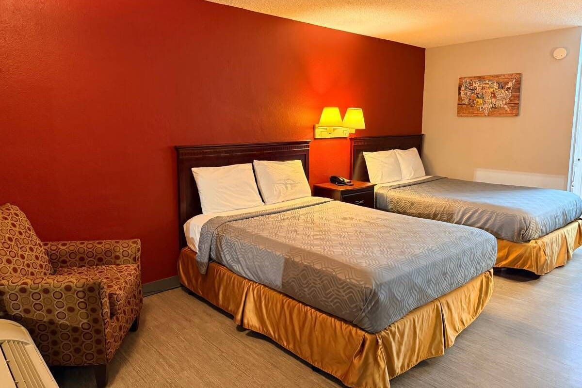 A hotel room with two beds, a chair, and a nightstand.