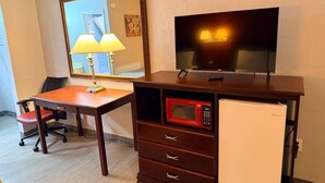 Une chambre d’hôtel compacte comprenant un bureau en bois, un four à micro-ondes, un mini-réfrigérateur, une télévision et un miroir.