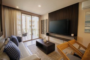 Una sala moderna con un televisor de pantalla plana grande, un sofá con cojines a rayas, una mesa de centro y una silla de madera.