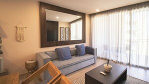 A modern living room with a grey sofa, striped cushions, a wooden coffee table, and a large mirror above the sofa. - Stay & Relax: Fully Equipped Loft in Los Cabos (Cabo San Lucas)