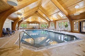 Une piscine intérieure dotée d’un plafond en bois, de chaises longues et offrant une vue sur l’extérieur.