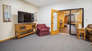 A living room with a flat-screen TV, a wooden cabinet, a red armchair, and a brown leather sofa. - Ski-in queen hotel room with pool, hot tub, and Wi-Fi. (Killington)