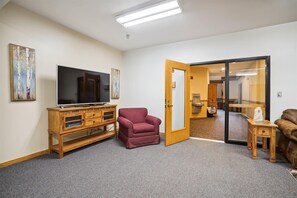 A living room with a flat-screen TV, a wooden cabinet, a red armchair, and a brown leather sofa. - Ski-in queen hotel room with pool, hot tub, and Wi-Fi. (Killington)