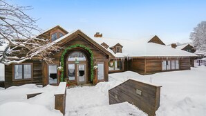 A wooden lodge with a snow-covered roof and a welcoming entrance adorned with greenery. - Ski-in queen hotel room with pool, hot tub, and Wi-Fi. (Killington)