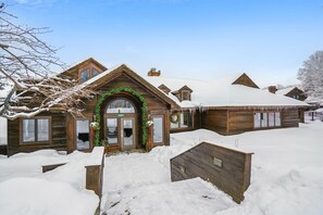 Un chalet en bois, dont le toit est recouvert de neige, et dont l’entrée accueillante est agrémentée de verdure.