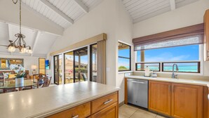 A spacious kitchen with wooden cabinets, a large island, and a view of the ocean. - Luxurious Wailea Oceanview Resort Vistas (Kihei)