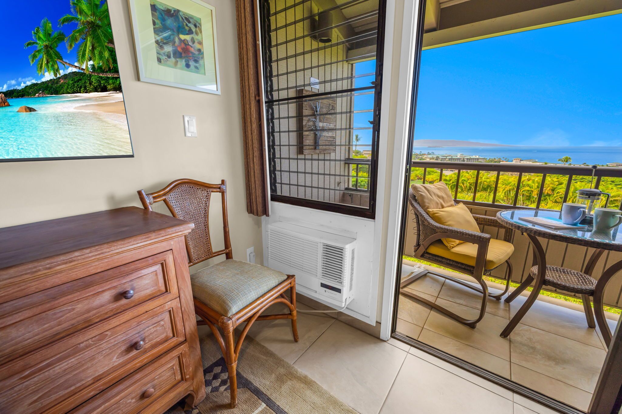 A balcony with wicker furniture, a wooden dresser, and a framed picture of a beach scene.