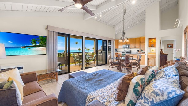 A spacious living area with a large bed, a sofa, and a dining table. There is a balcony with a view of the ocean. - Luxurious Wailea Oceanview Resort Vistas (Kihei)