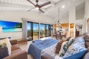 En rummelig opholdsstue med en stor seng, sofa og spisebord. Der er en balkon med udsigt over havet.