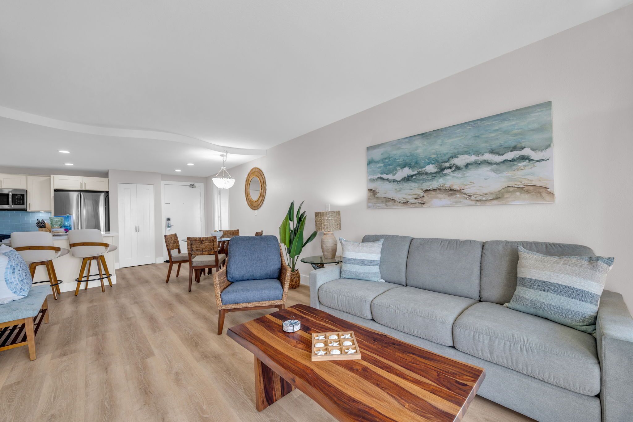 A modern living room with a grey sofa, wooden coffee table, and a painting of waves on the wall.