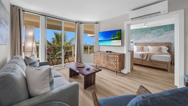 Een moderne woonkamer met een bank, een salontafel, een televisie, een bed en een balkon met uitzicht op de oceaan.