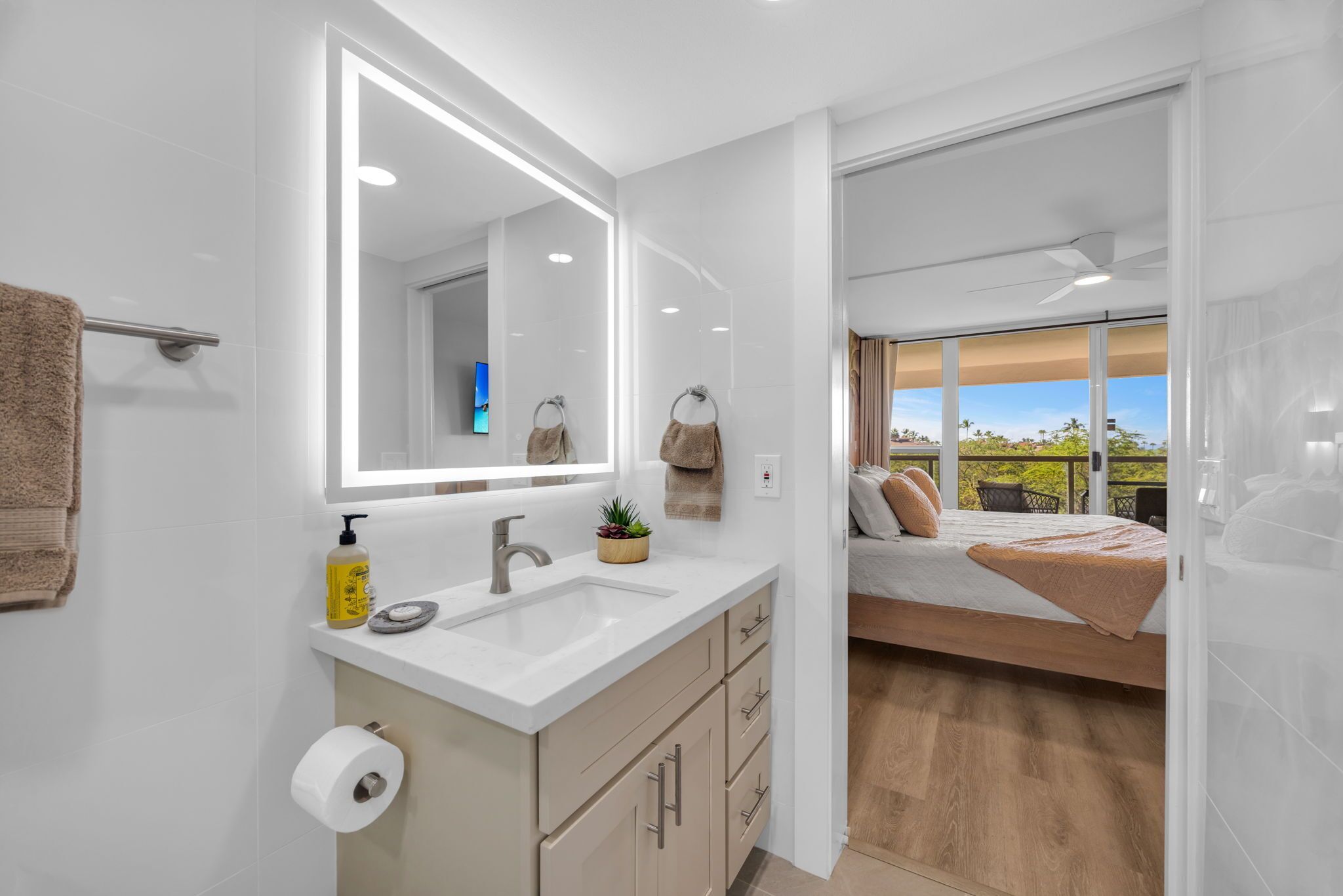 Un baño moderno con un espejo grande, lavamanos blanco y armarios color beige.