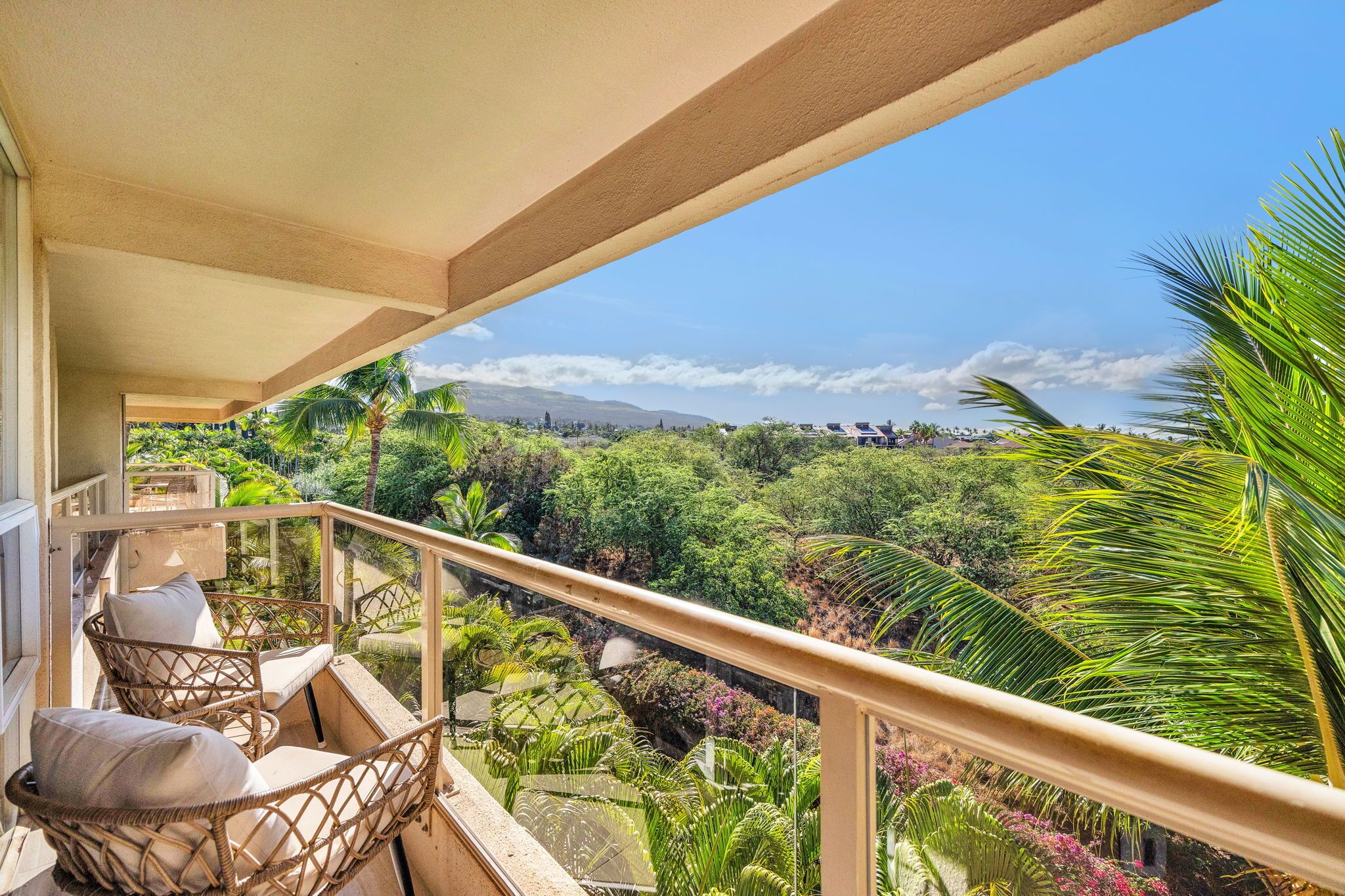 A balcony with wicker chairs and a view of lush greenery and distant mountains.