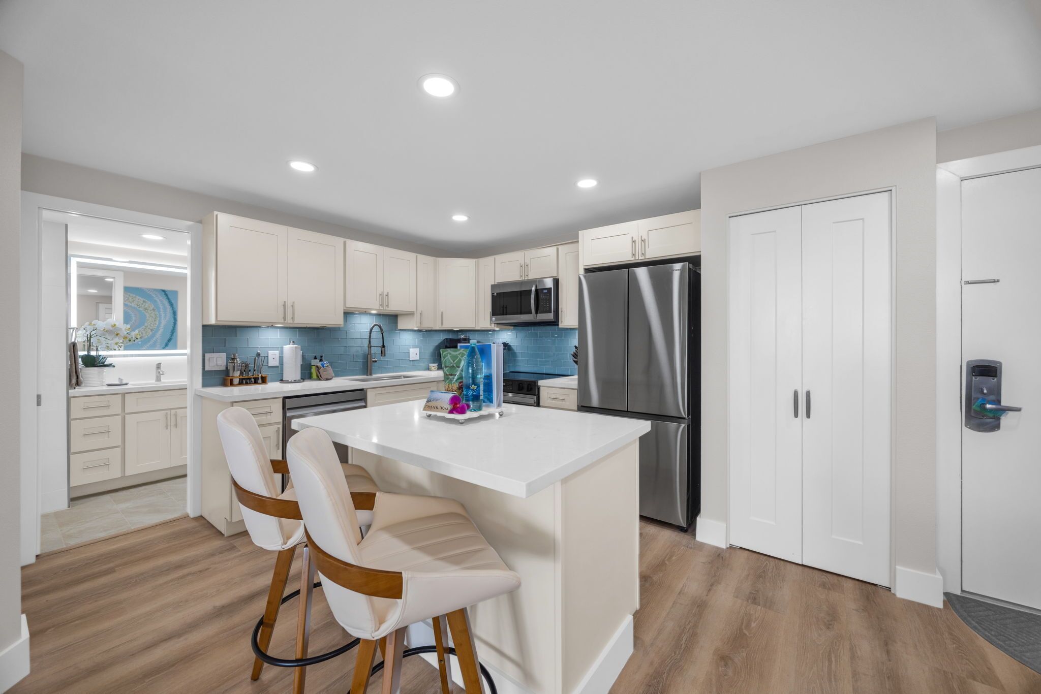 A modern kitchen with white cabinets, stainless steel appliances, and a central island with bar stools.