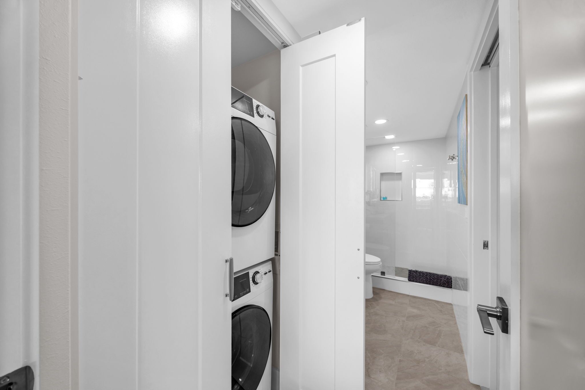 Een moderne wasruimte met gestapelde wasmachines en drogers, een toilet en een douche.