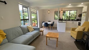 Ein modernes Wohnzimmer mit einer Couch, einem Couchtisch und gelben Sessel. Es gibt einen Essbereich mit Tisch und Stühlen sowie eine Küche mit Kühlschrank und Mikrowelle.