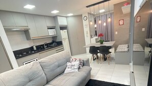 A modern living room with a grey sofa, black rug, and a dining area with a table and chairs.