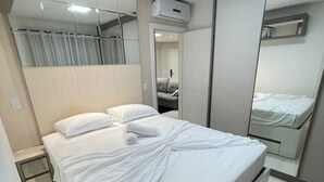 A modern bedroom with a large bed, a bedside table, a mirror, and an air conditioning unit.