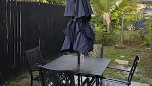 Une terrasse extérieure avec une table et des chaises, entourée d’une clôture noire et de palmiers.