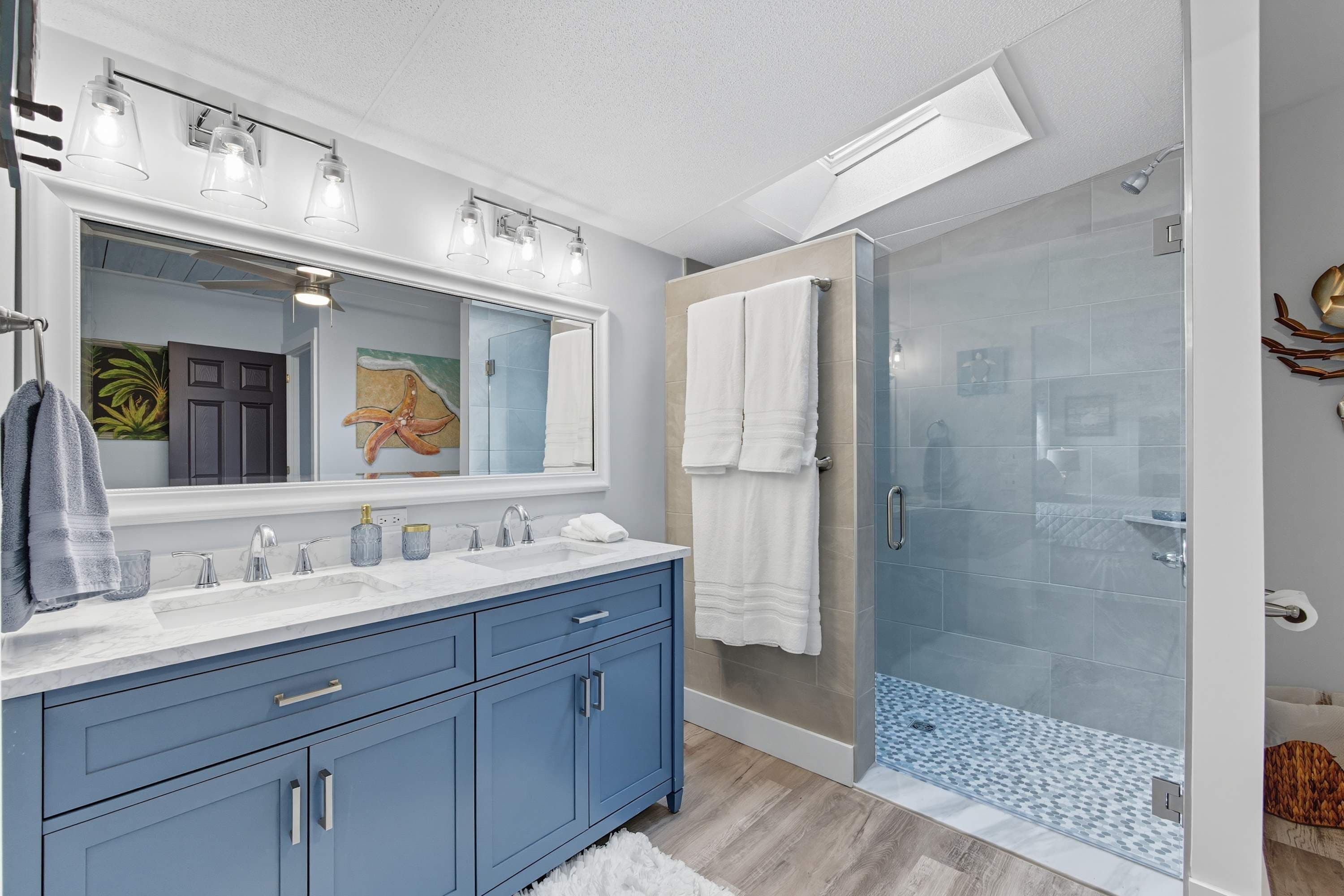 Un baño moderno con un espejo grande, lavamanos dobles y una ducha con cerramiento de vidrio.