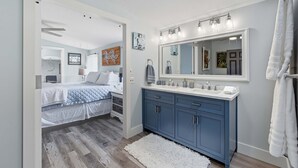 Een slaapkamer met een bed, een badkamer met een wastafel en spiegel, en een witte vloerkleed.