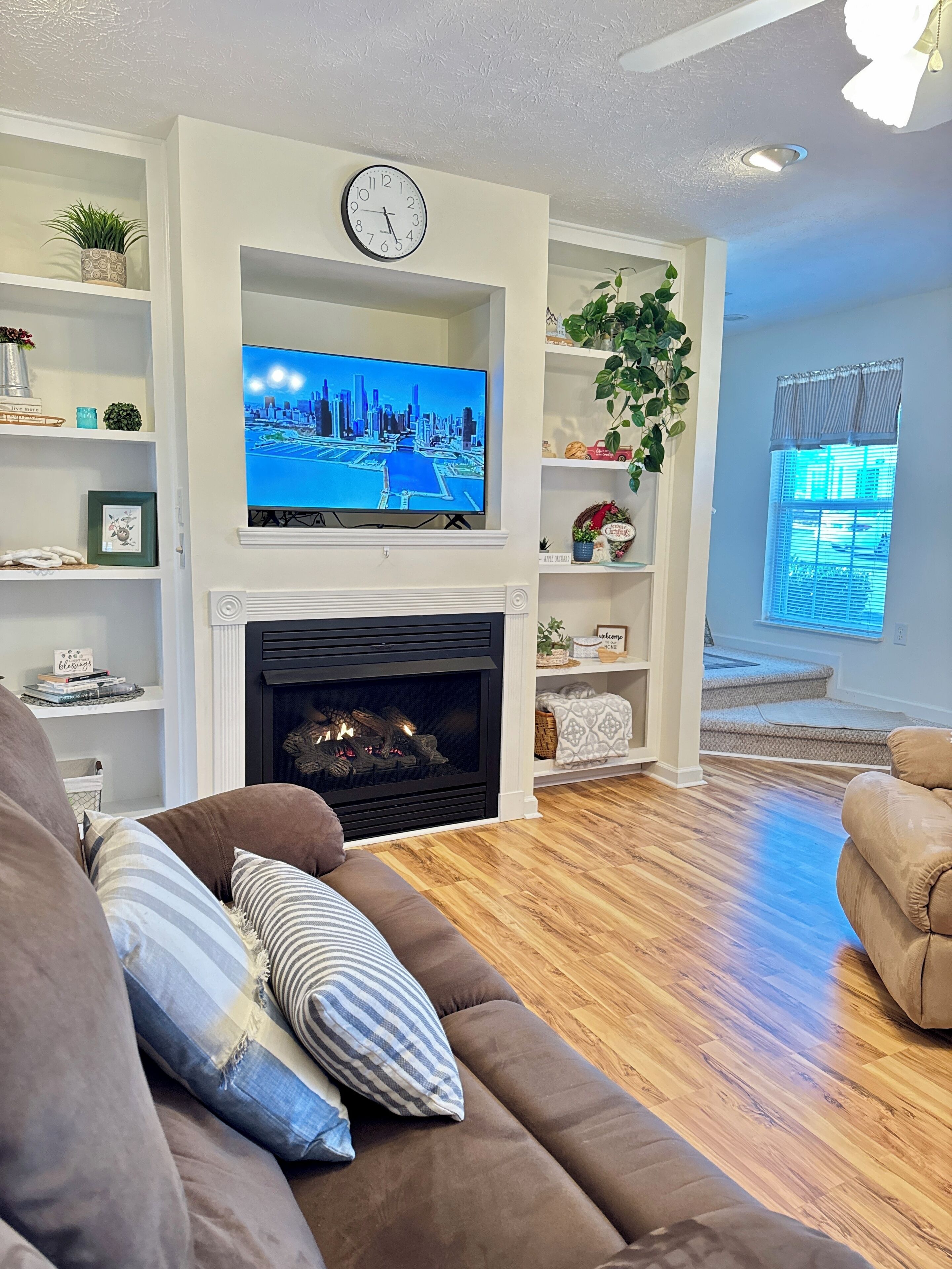 A living room with a fireplace, a television, and a clock on the wall.