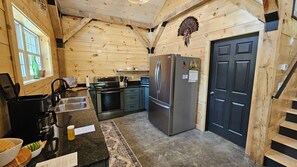 A wooden interior with a kitchen, including a refrigerator, stove, and sink. - Larch - The Tamaracks - Outdoor Adventures Aroostook County (Caribou)