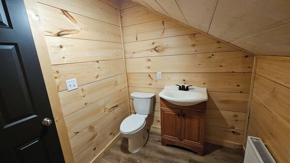 A small, wooden-paneled bathroom with a toilet and a sink.