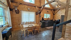 A wooden cabin interior with a dining table, chairs, a kitchen area, and a staircase. - Larch - The Tamaracks - Outdoor Adventures Aroostook County (Caribou)