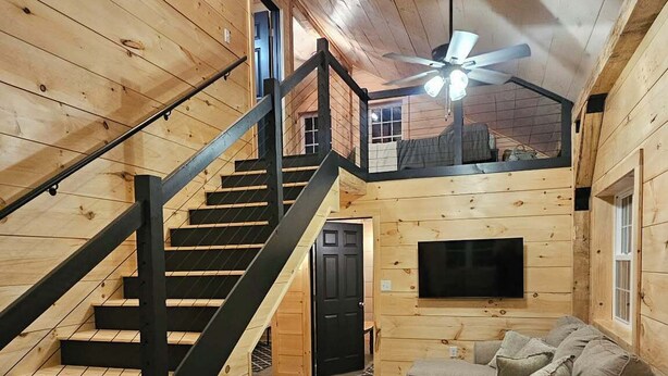 L’intérieur d’une cabane en bois comprend un escalier, un espace de vie avec un canapé et une table, ainsi qu’un ventilateur de plafond.