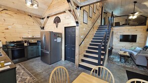 A cabin interior with a kitchen, dining area, and a staircase. - Larch - The Tamaracks - Outdoor Adventures Aroostook County (Caribou)