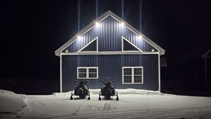 Une maison bleu foncé, avec un toit à pignon et deux fenêtres, entourée de neige.