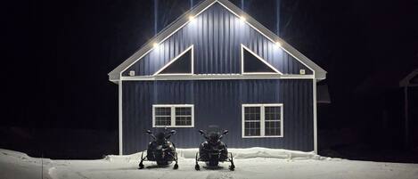 Una casa azul oscuro con techo a dos aguas y dos ventanas, rodeada de nieve.