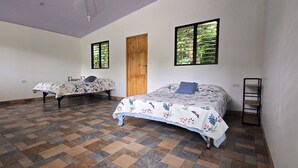 A room with two beds, a wooden door, and a window with a view of greenery. - Savegre River Cabina + Mediterranean Food (Savegre)