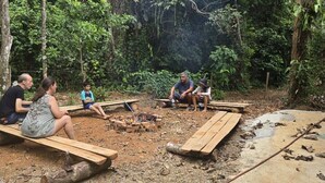 A group of people sitting on wooden benches around a campfire in a forested area. - Savegre River Cabina + Mediterranean Food (Savegre)