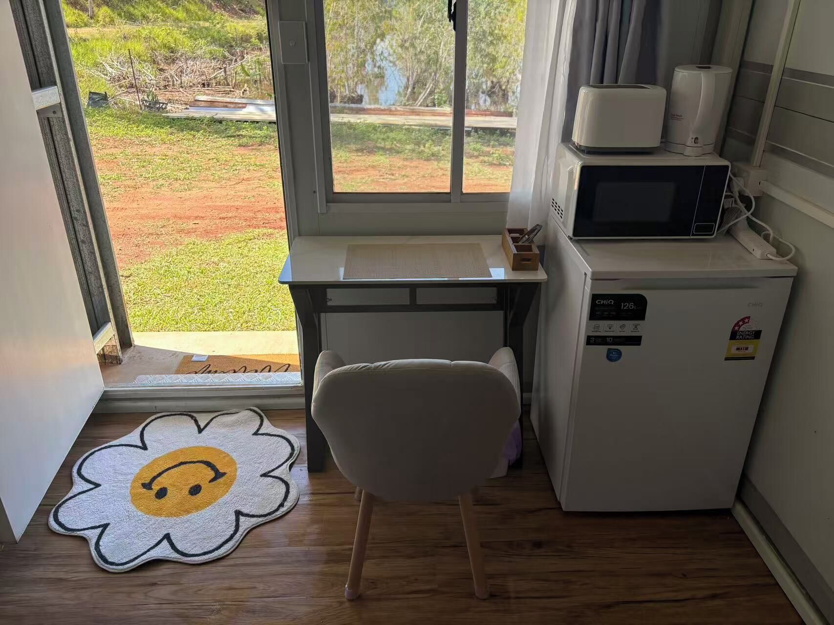 A small kitchenette with a microwave, refrigerator, and a window with a view of a garden.