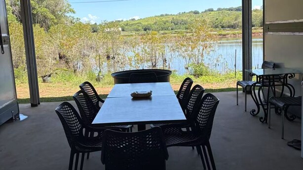 Une terrasse extérieure avec une table et des chaises, un ventilateur de plafond et une vue sur un lac et la verdure.