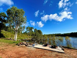 A lakeside picnic area with a concrete table and chairs, surrounded by trees and a clear sky.