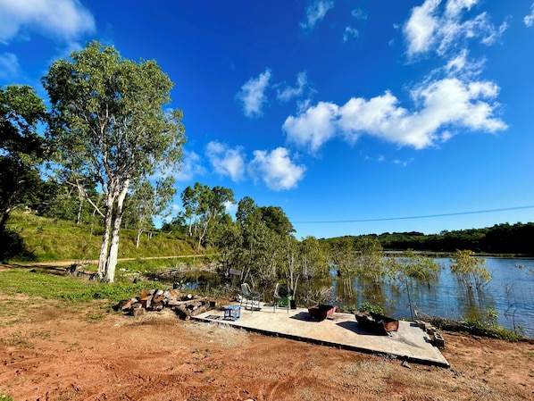 A lakeside picnic area with a concrete table and chairs, surrounded by trees and a clear sky.