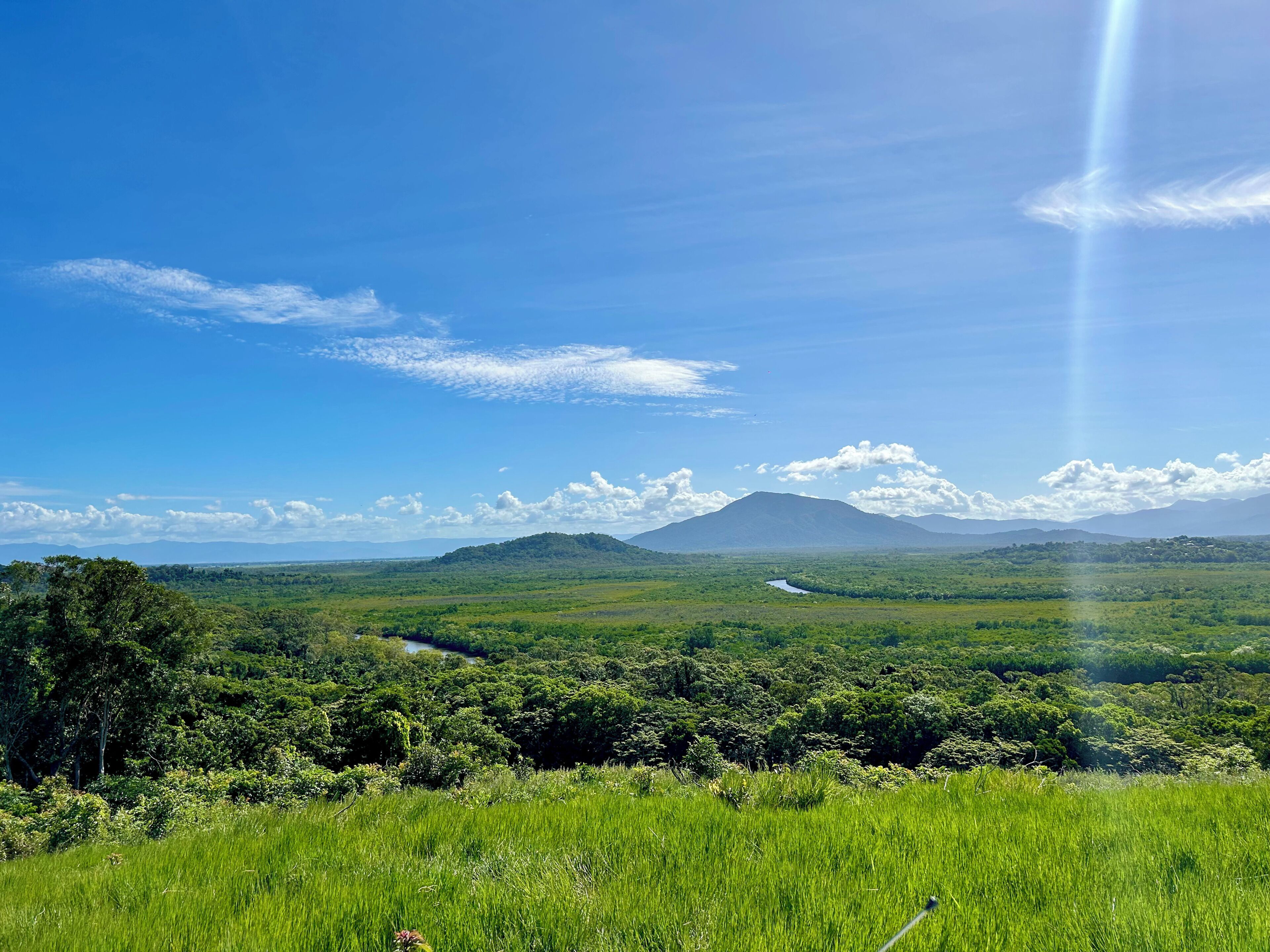 A landscape with a river, green fields, and distant mountains.