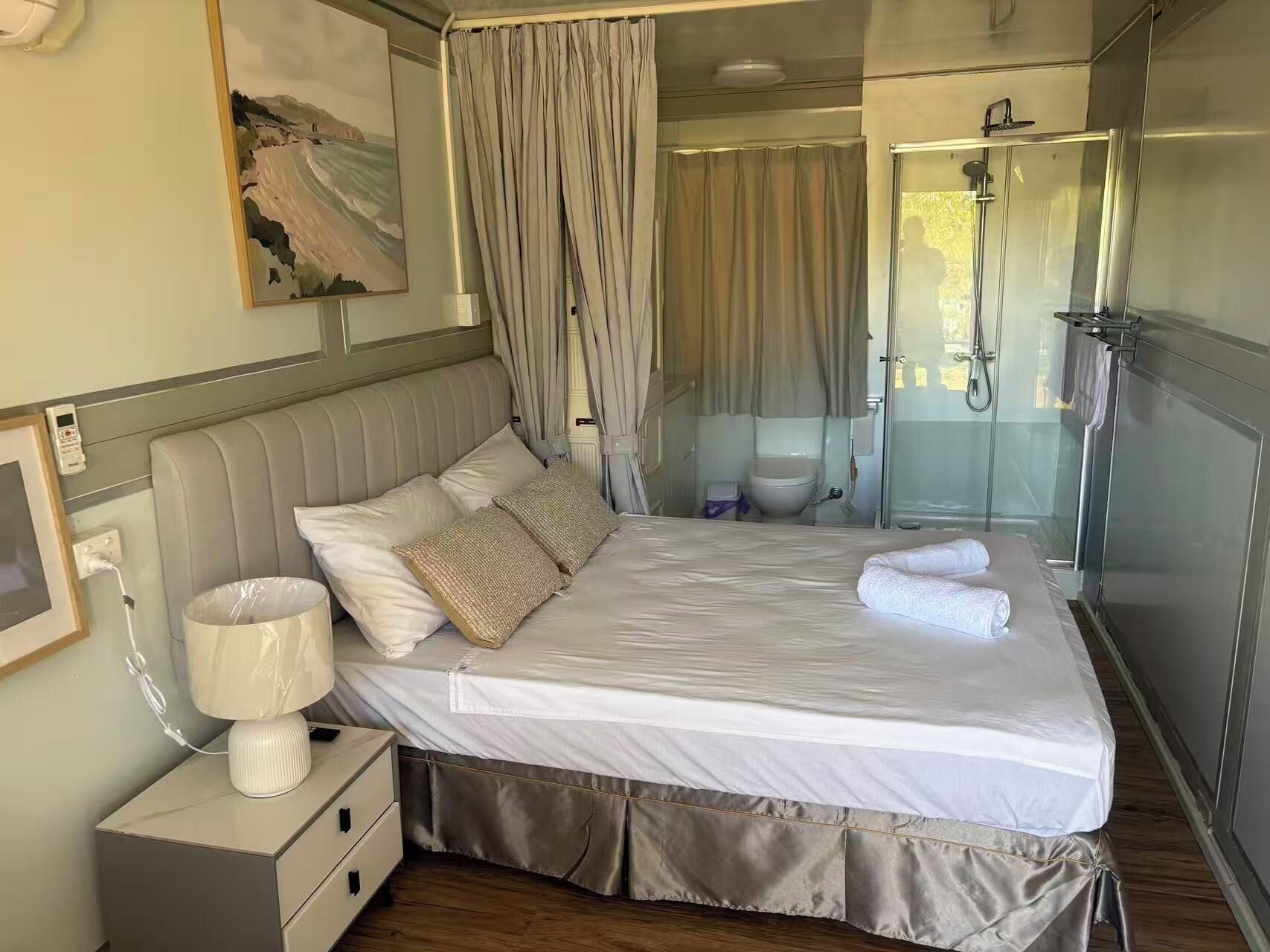Habitación de hotel con cama, lámpara de noche y zona de ducha.