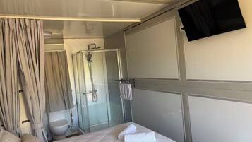A hotel room with a bed, a shower, a toilet, and a TV mounted on the wall.